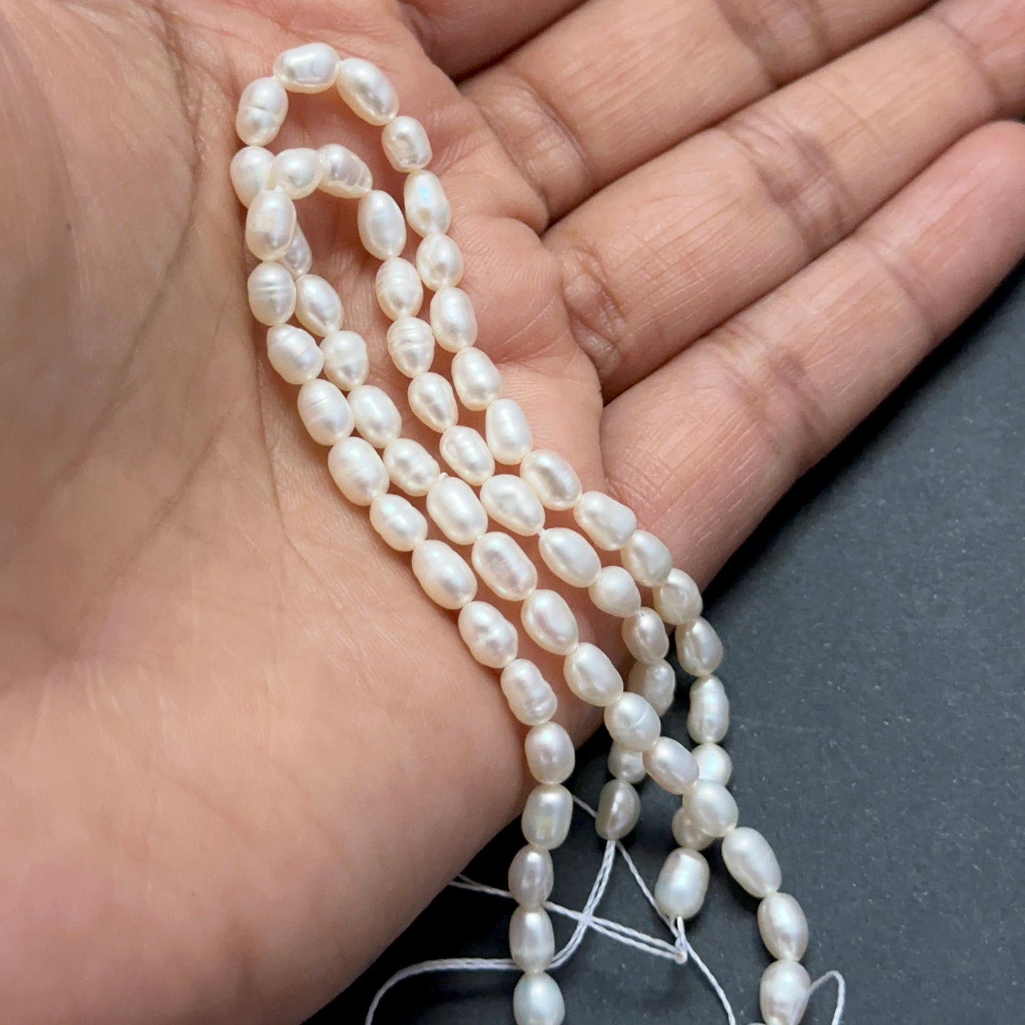 A person holds delicate strands of Freshwater Pearls beads, showcasing their smooth design.