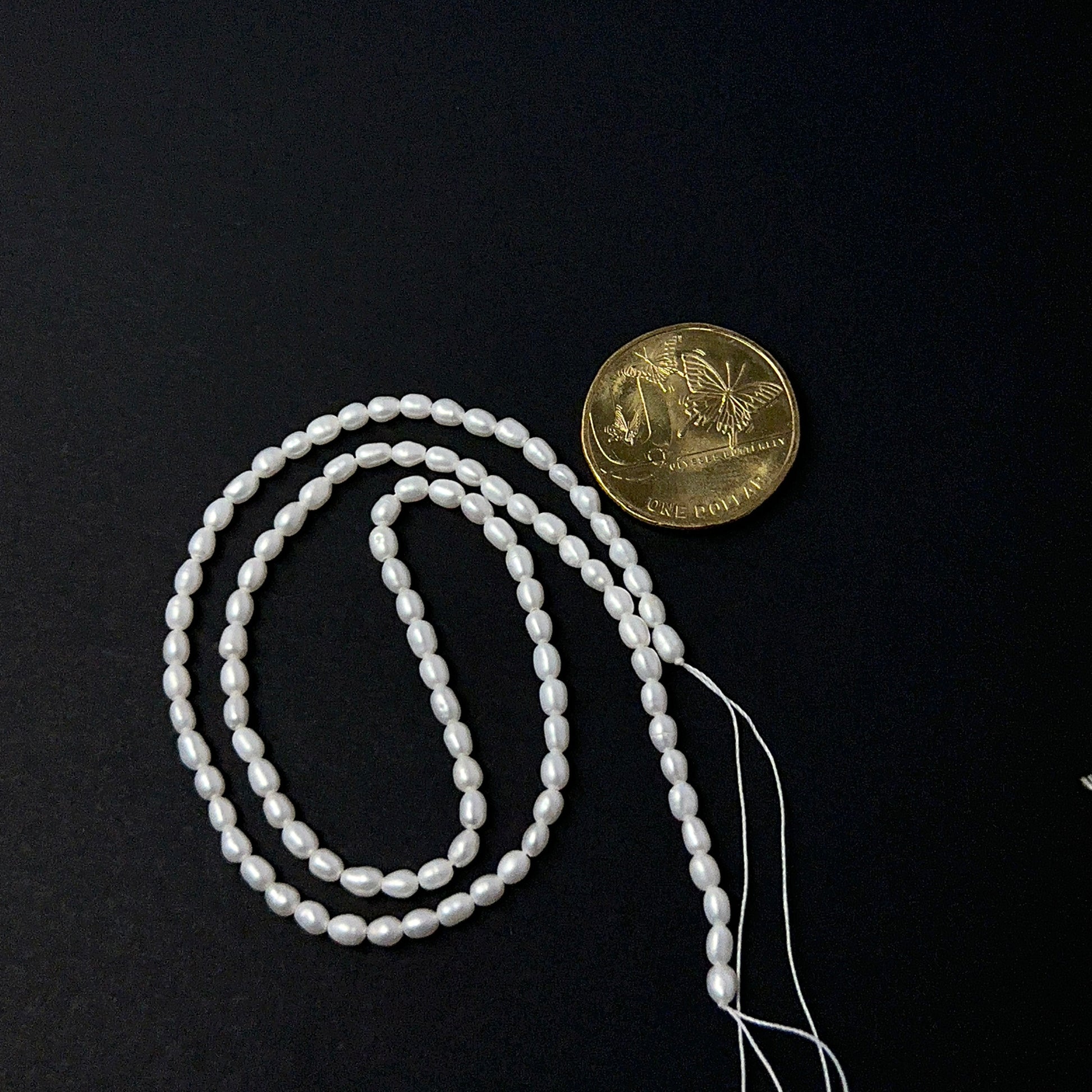 A coin is place near delicate strands of Freshwater Pearl beads for scale.
