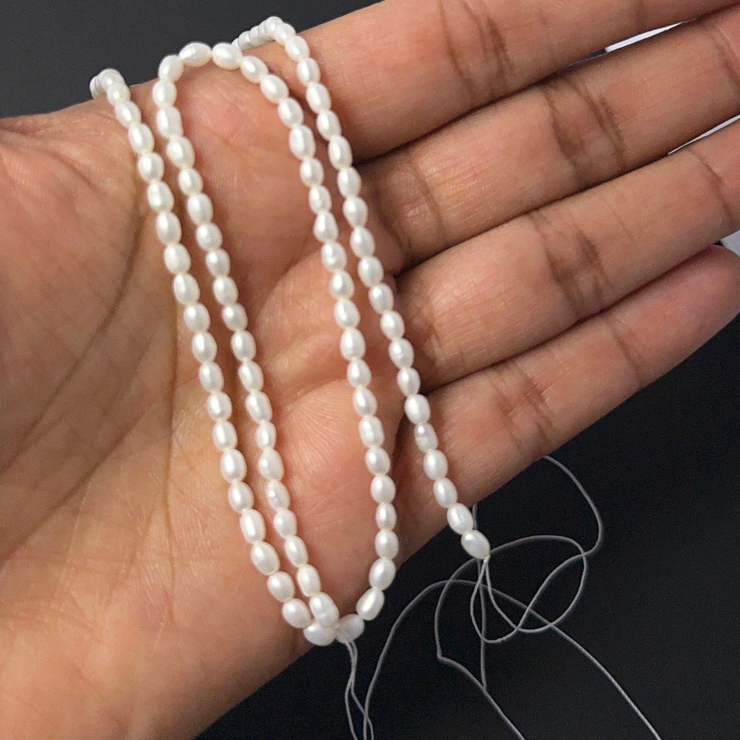A person holds delicate strands of Freshwater Pearl beads, showcasing their smooth rice design.