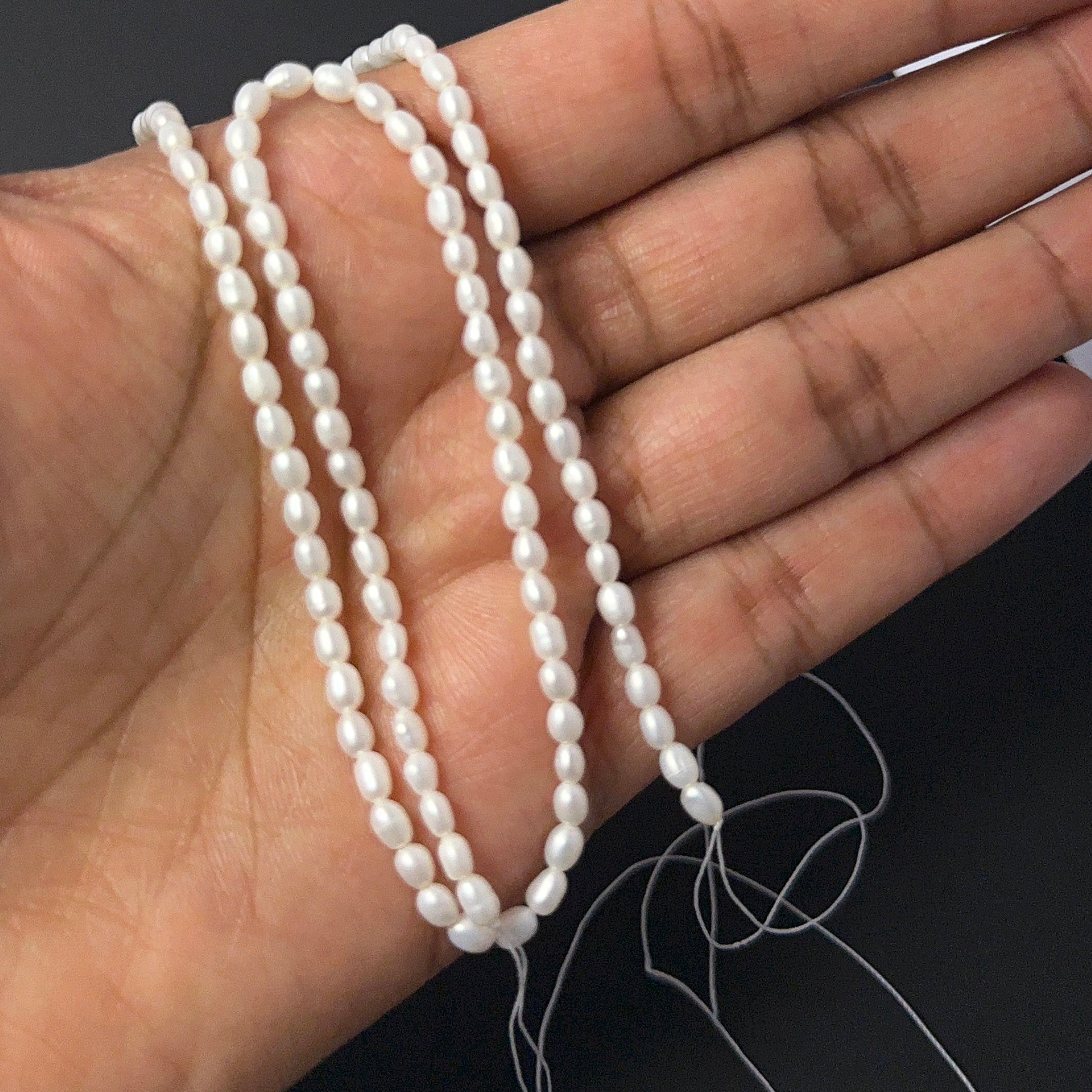 A person holds delicate strands of Freshwater Pearl beads, showcasing their smooth rice design.