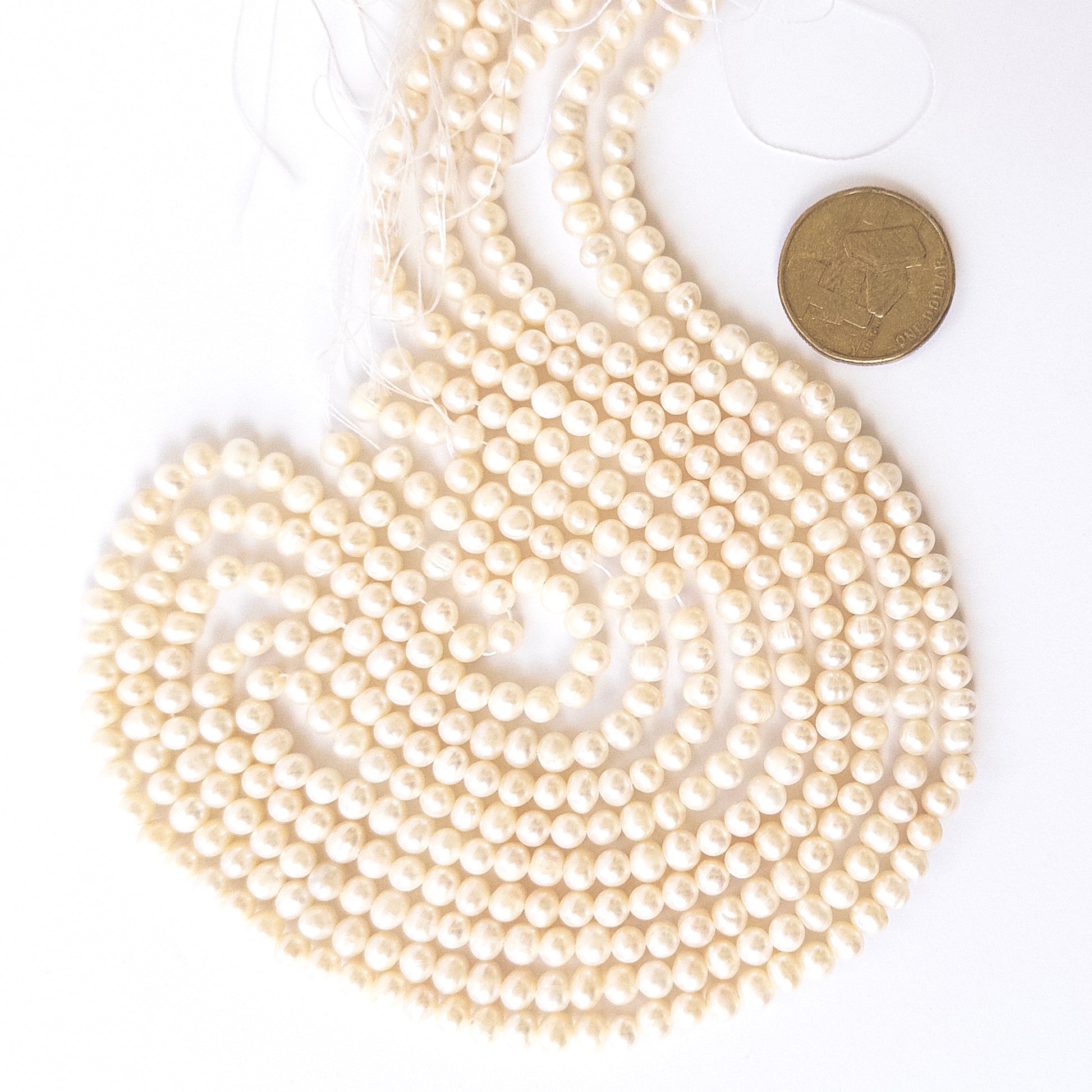 A coin is place near delicate strands of Freshwater Pearls beads for scale.
