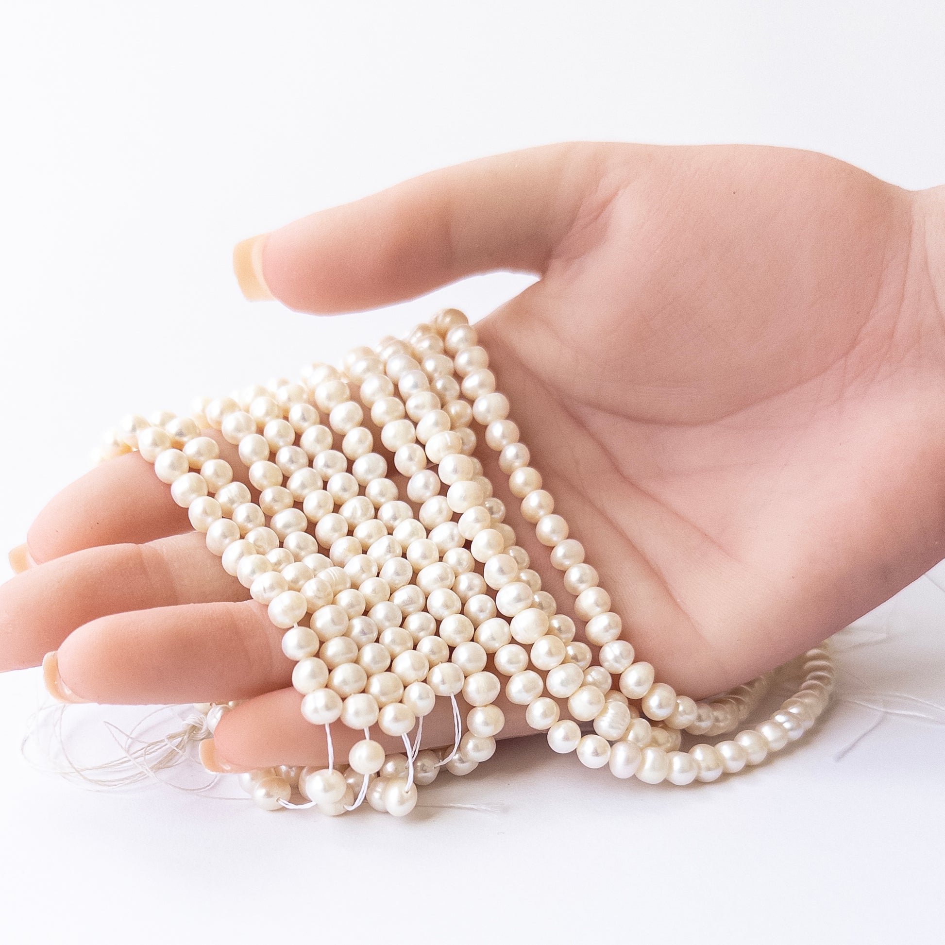 A person holds delicate strands of Freshwater Pearls beads, showcasing their smooth rondelle design.