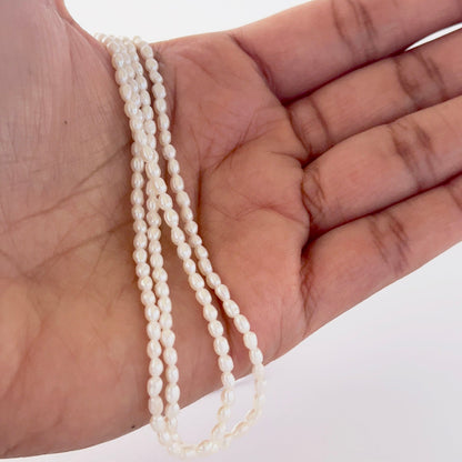 A person holds delicate strands of freshwater rice pearls, showcasing their natural shape.