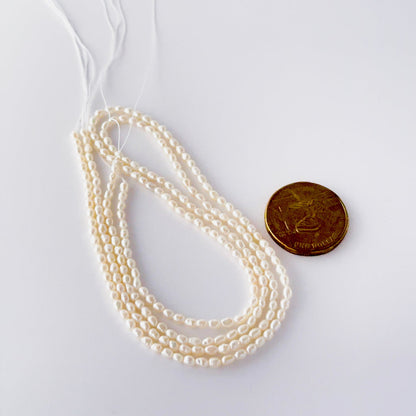 A coin is placed near delicate strands of freshwater rice pearls for scale.