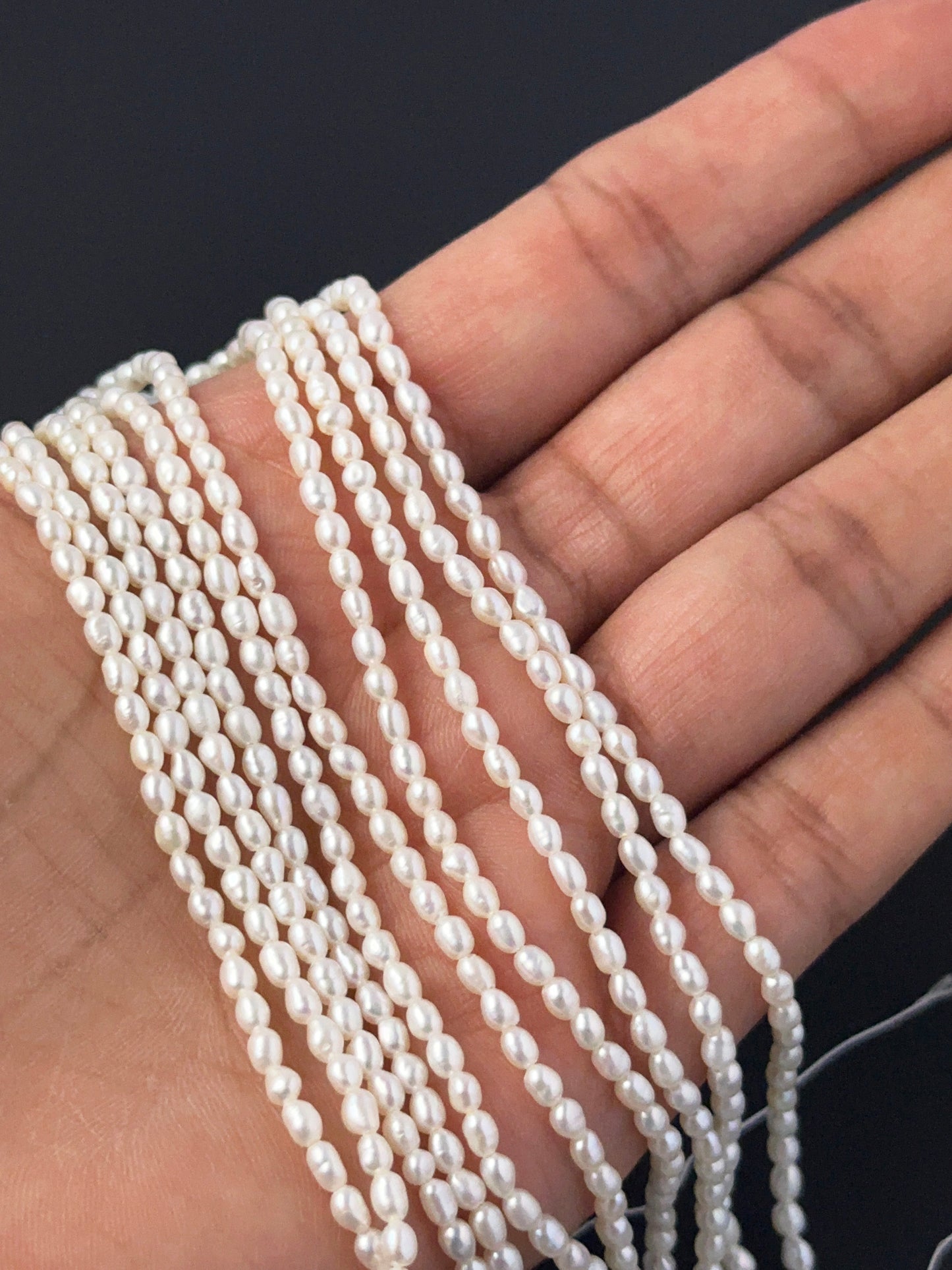 A person holds delicate strands of freshwater rice pearl beads, showcasing their smooth design.
