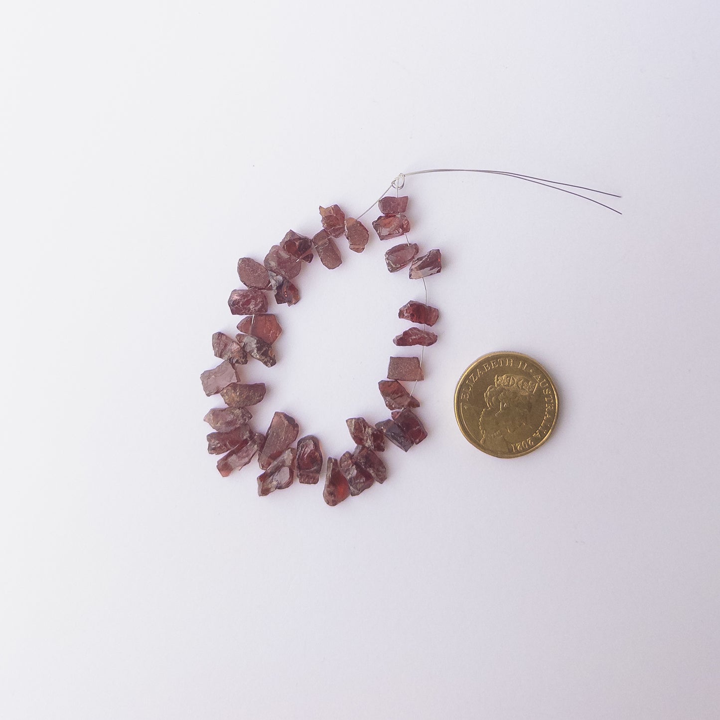 A coin is place near delicate pieces of Garnet beads for scale.