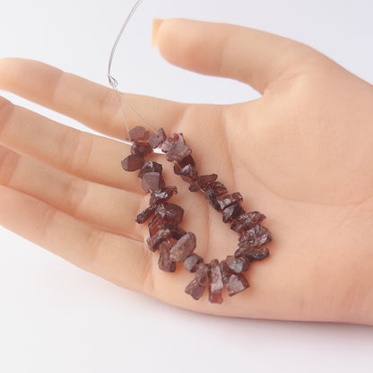 A person holds delicate strands of Garnet beads, showcasing their drilled rough design.