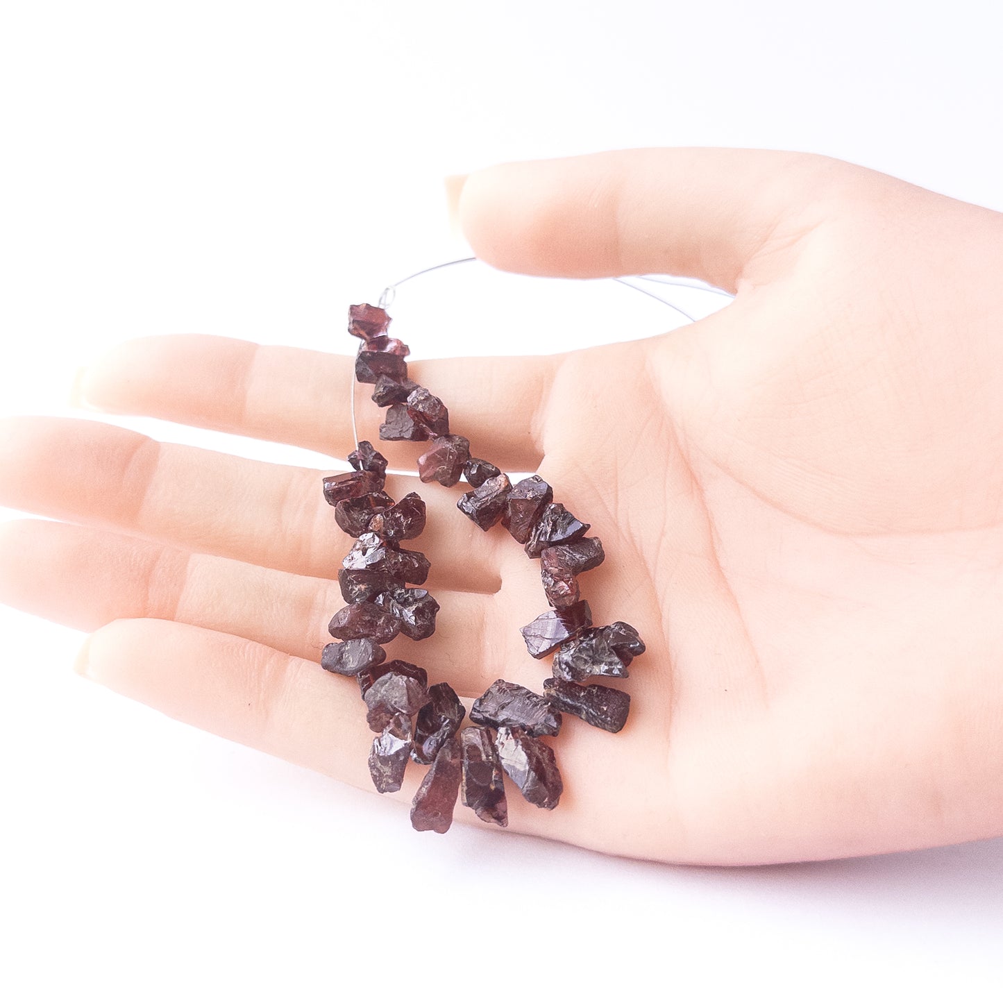 A person holds delicate strands of Garnet beads, showcasing their drilled rough design.