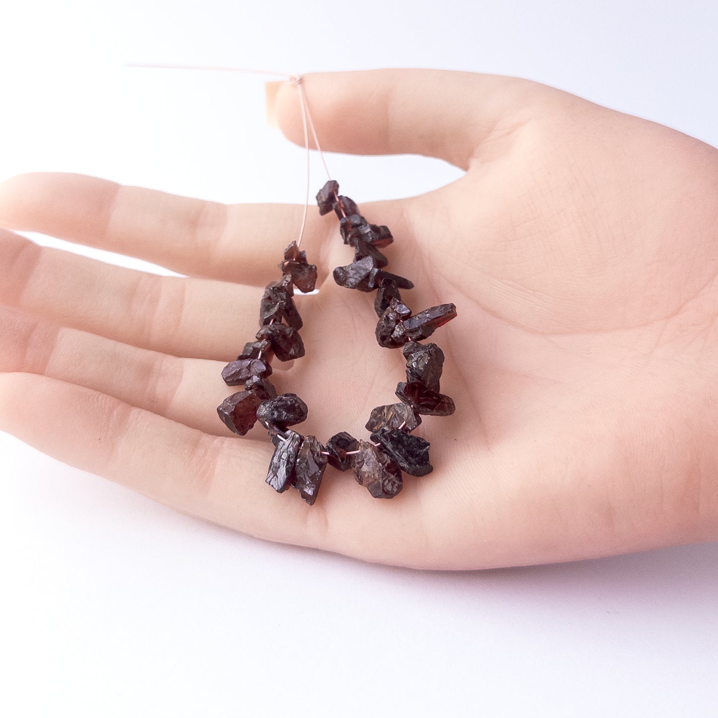 A person holds delicate strands of Garnet beads, showcasing their drilled rough design.