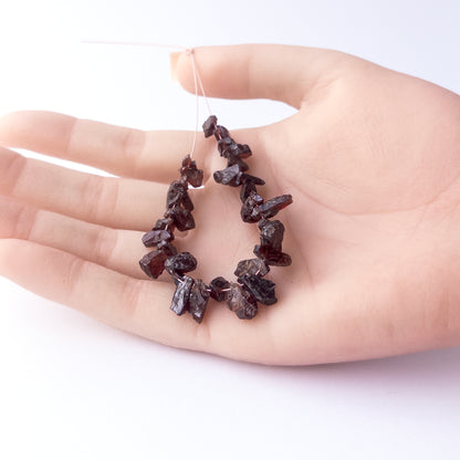 A person holds delicate strands of Garnet beads, showcasing their drilled rough design.