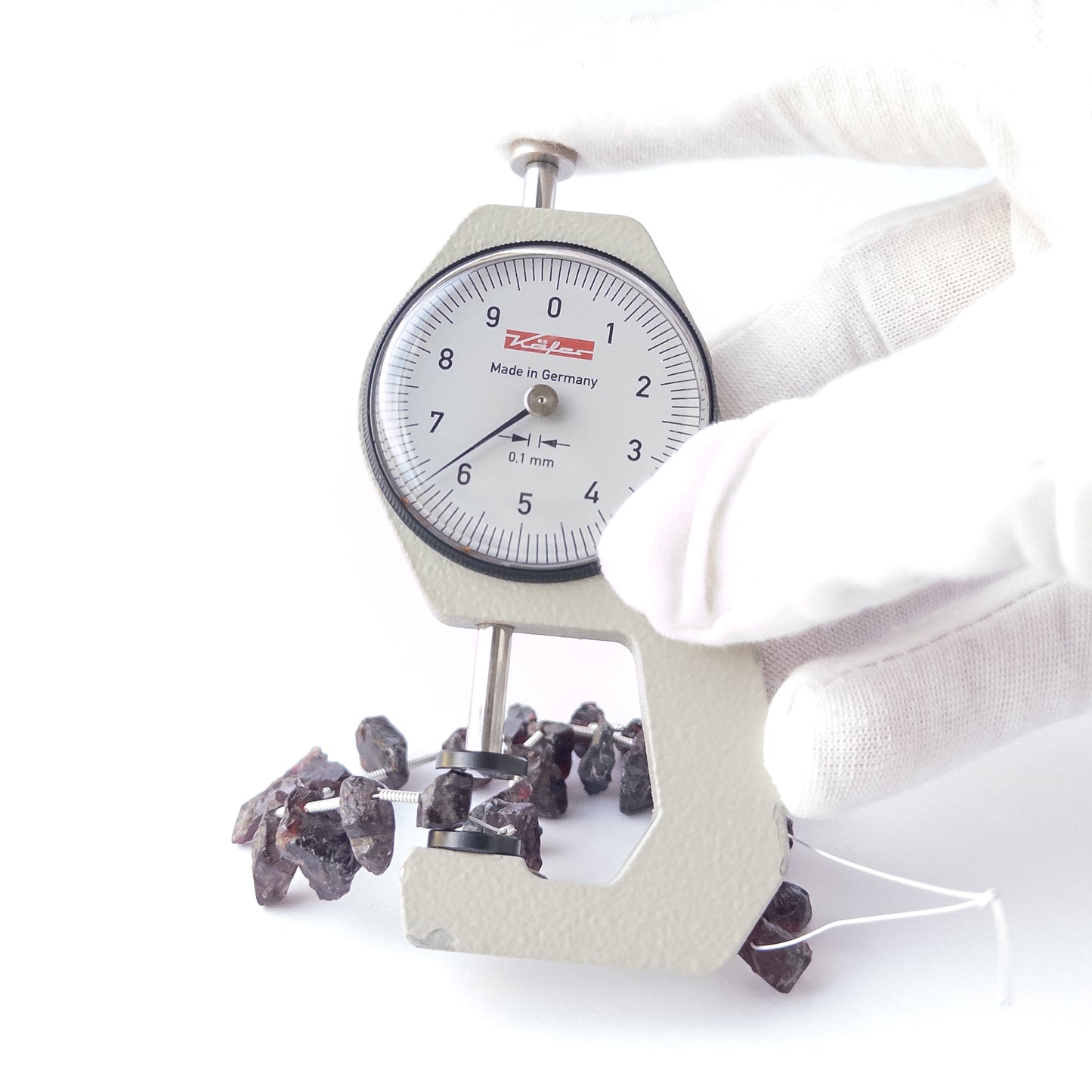 A dial gauge measures the Garnet drilled rough 6–7mm bead size gemstone.