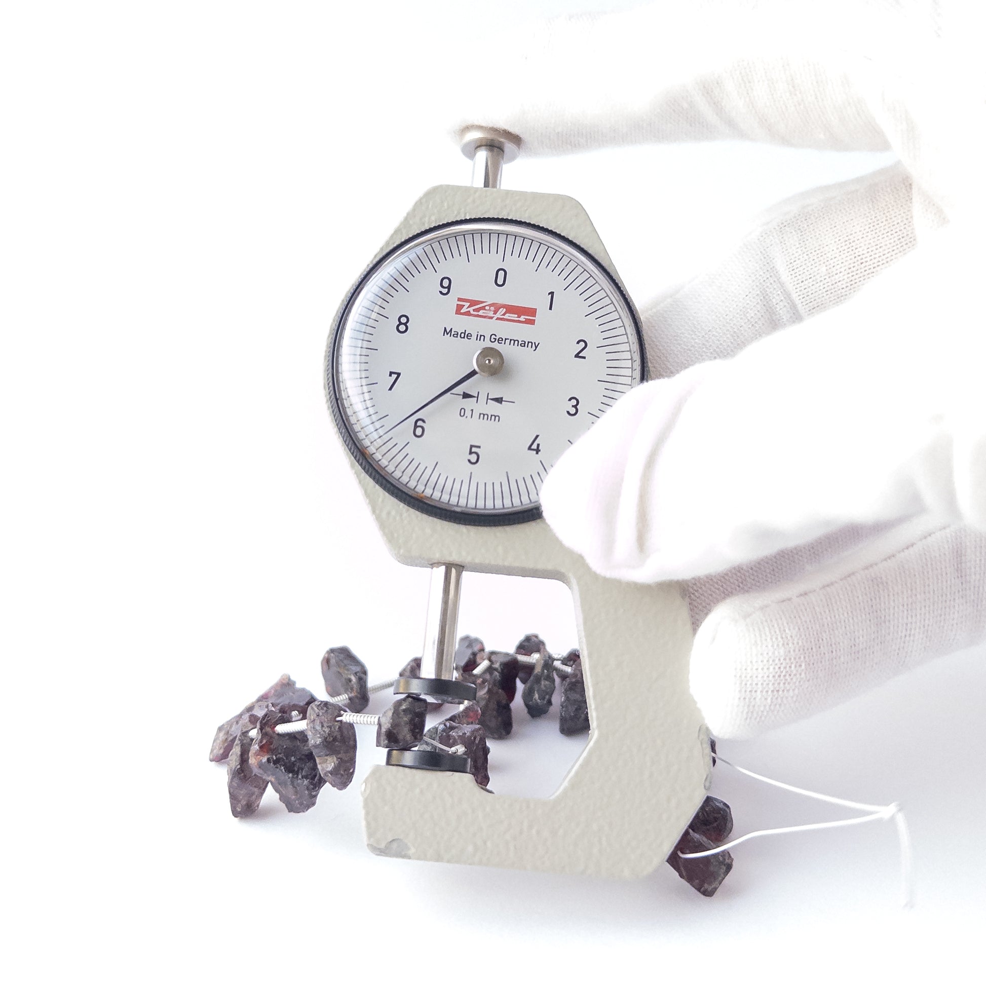A dial gauge measures the Garnet drilled rough 6–7mm bead size gemstone.