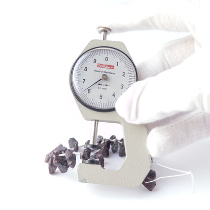A dial gauge measures the Garnet drilled rough 6–7mm bead size gemstone.