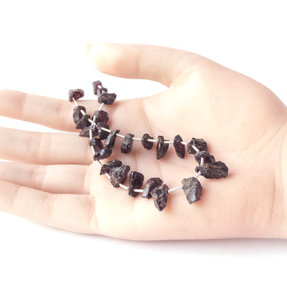 A person holds delicate strands of Garnet beads, showcasing their drilled rough design.