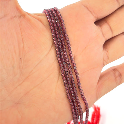 Hand holds small faceted Garnet rondelle beads in deep red hues on a 32cm strand

