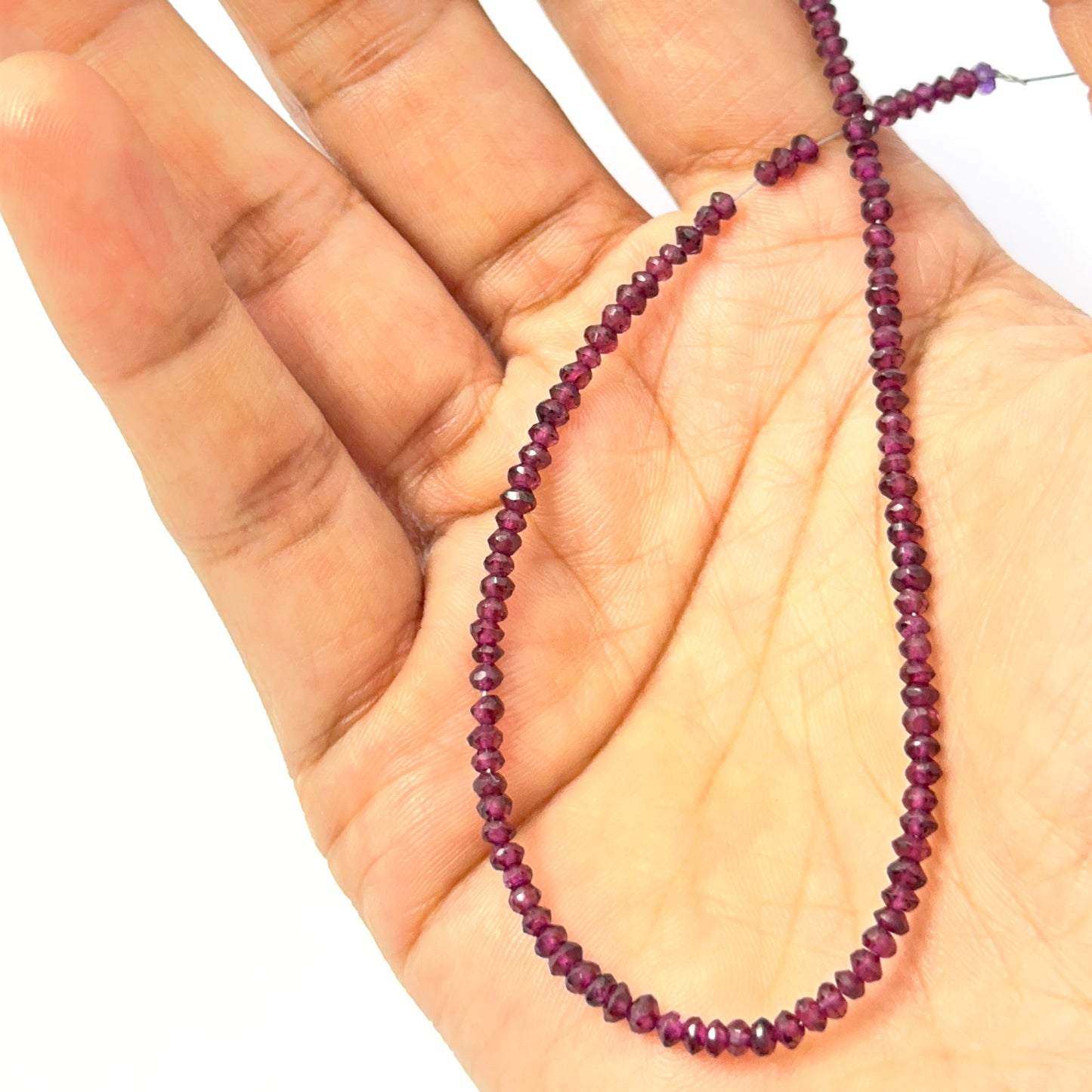 A person holds delicate strands of garnet beads, showcasing their faceted design.