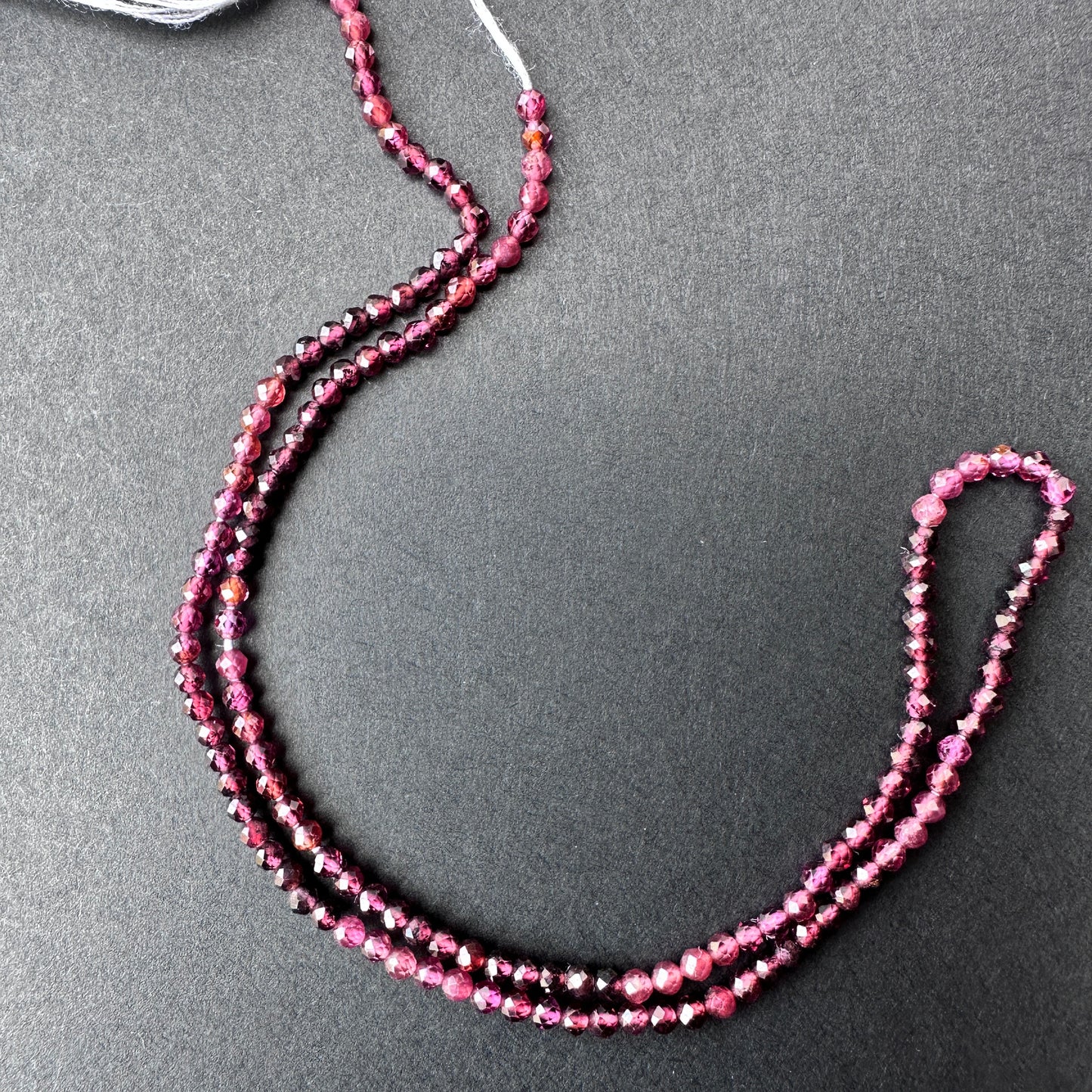 Close-up of garnet gemstone beads with glossy surface and uniform 2.4mm sizing for versatile jewellery making.