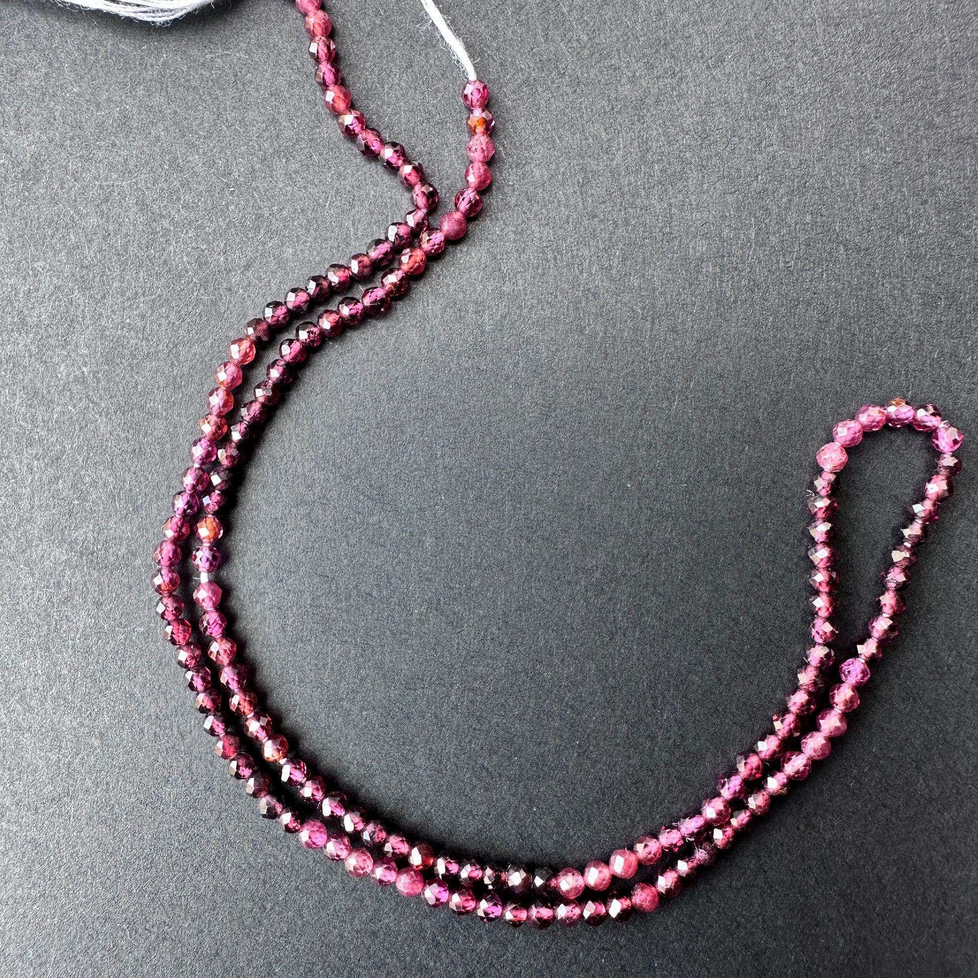 Close-up of garnet gemstone beads with glossy surface and uniform 2.4mm sizing for versatile jewellery making.