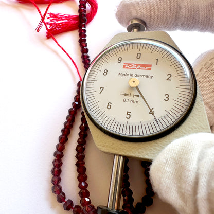 A dial gauge measures the Garnet faceted rondelle 4mm gemstone.