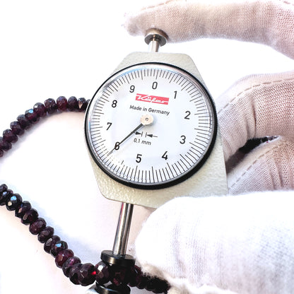 A dial gauge measures the Garnet faceted rondelle 6.0mm gemstone.
