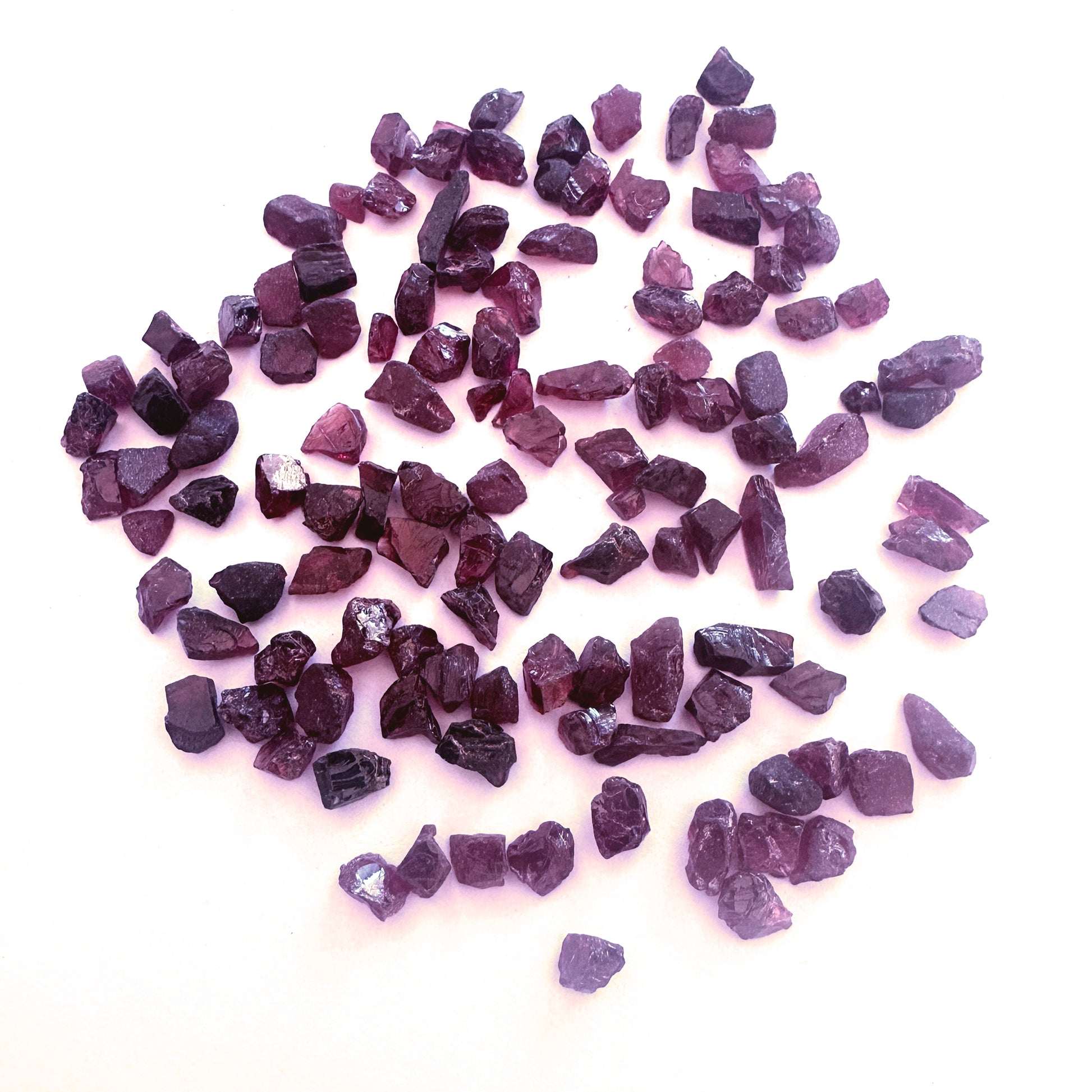 Undrilled garnet roughs arranged in a 20-piece set with earthy brilliance and varied shapes.