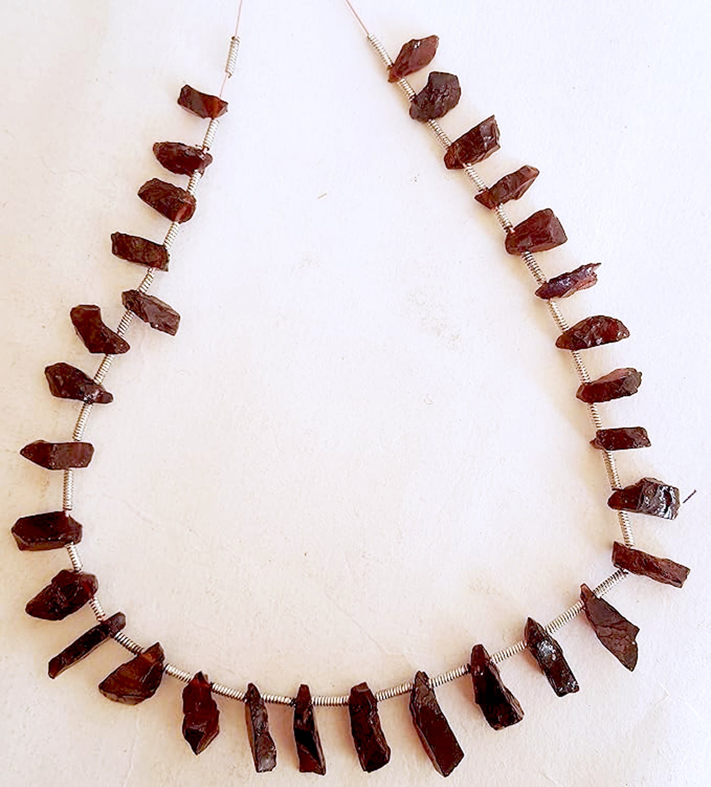 Deep red rough garnet beads arranged in a natural strand, showcasing raw texture and earthy brilliance.