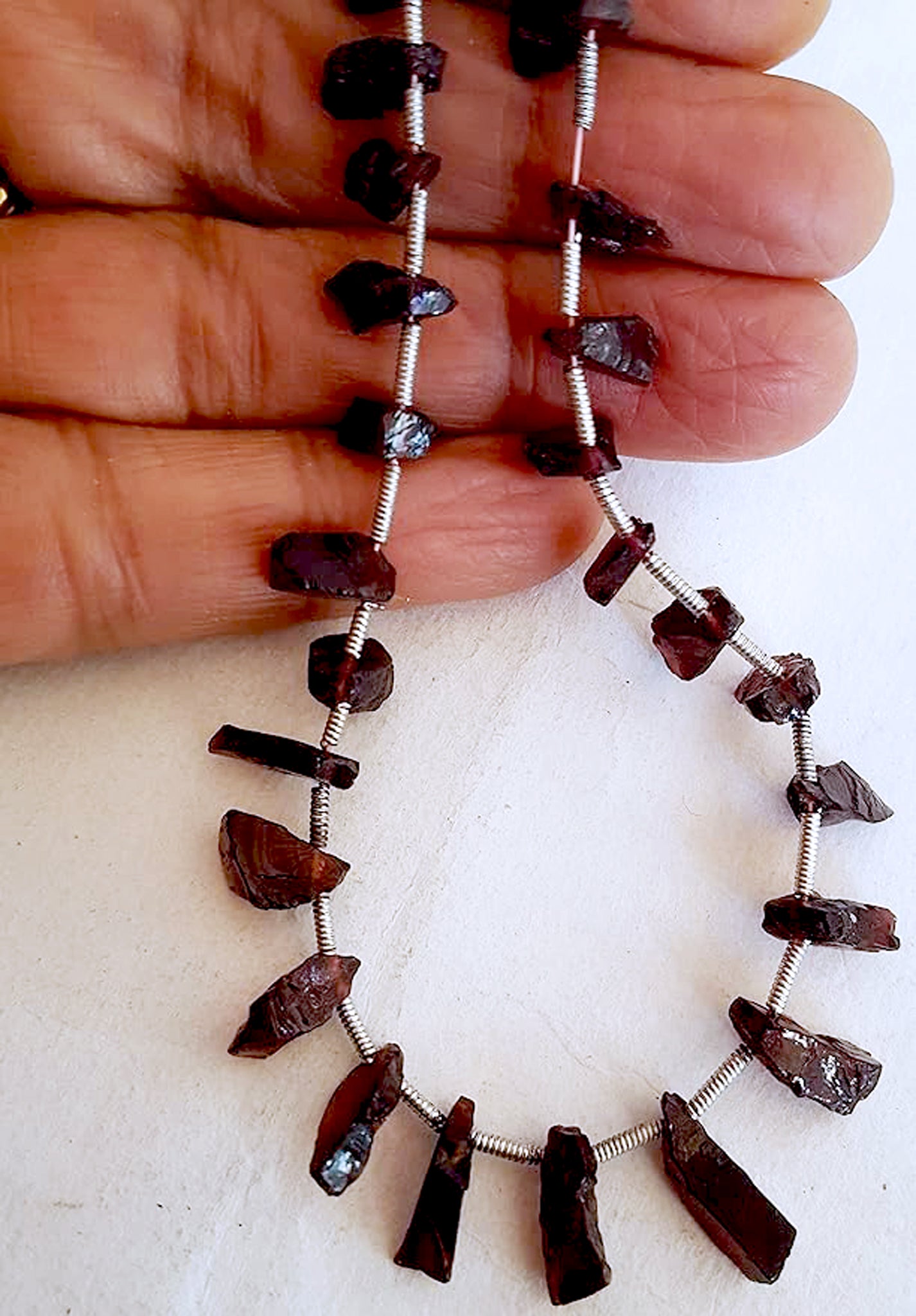 A person holds delicate strands of garnet beads, showcasing their rough natural state.