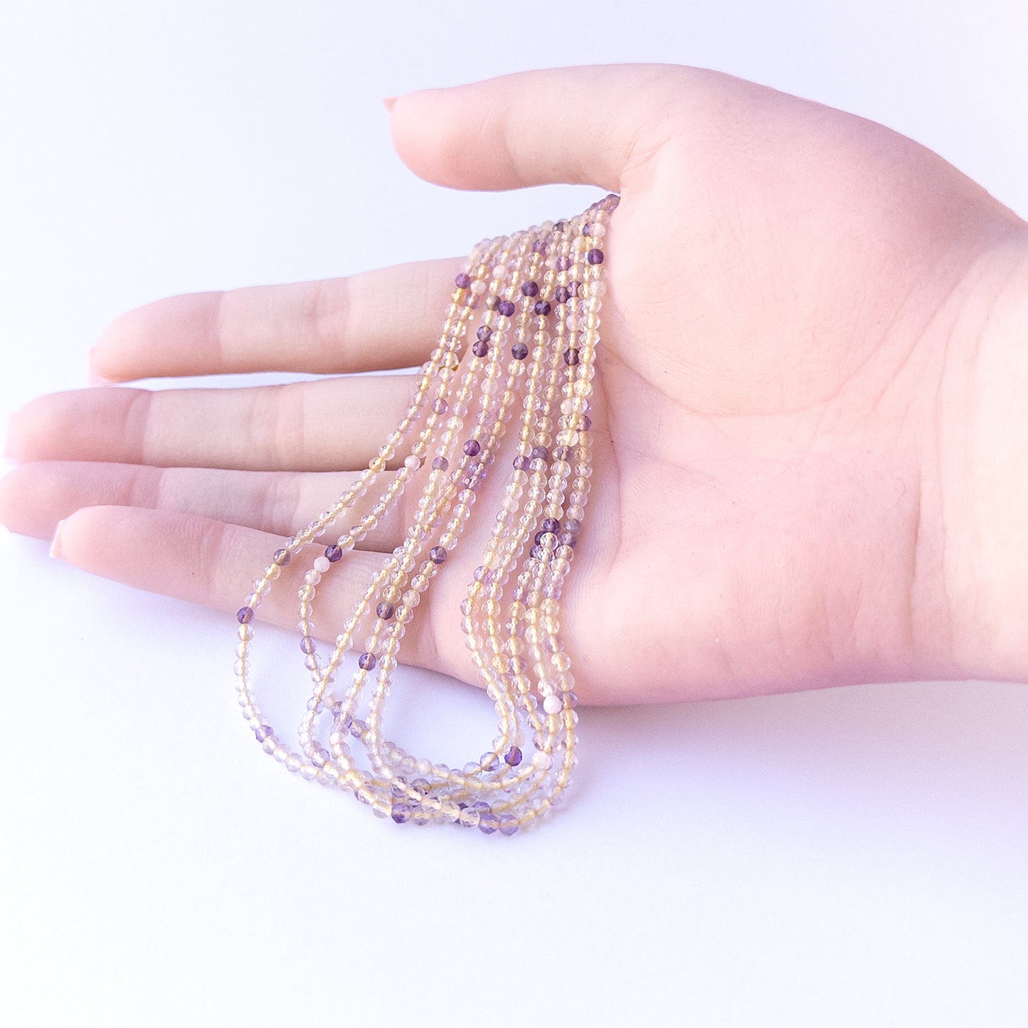 A person holds delicate strands of Golden Rutile beads, showcasing their faceted rondelle design.