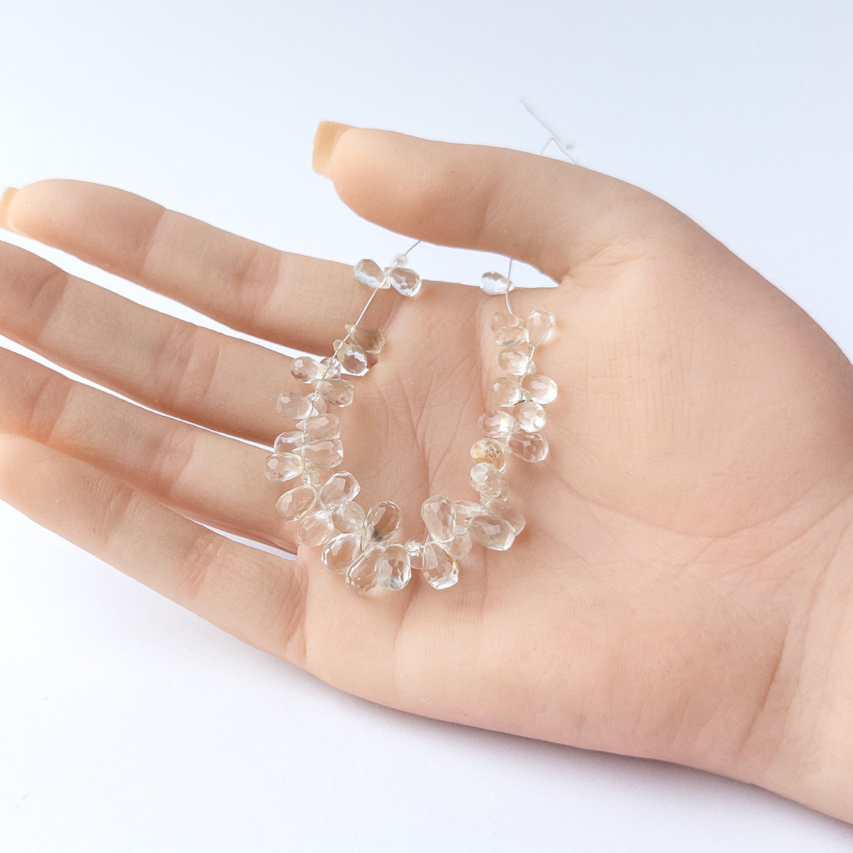 A person holds delicate pieces of Green Amethyst beads, showcasing their faceted briolette design.