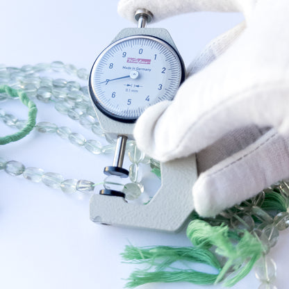 A dial gauge measures the Green Amethyst faceted oval 6–7mm gemstone.