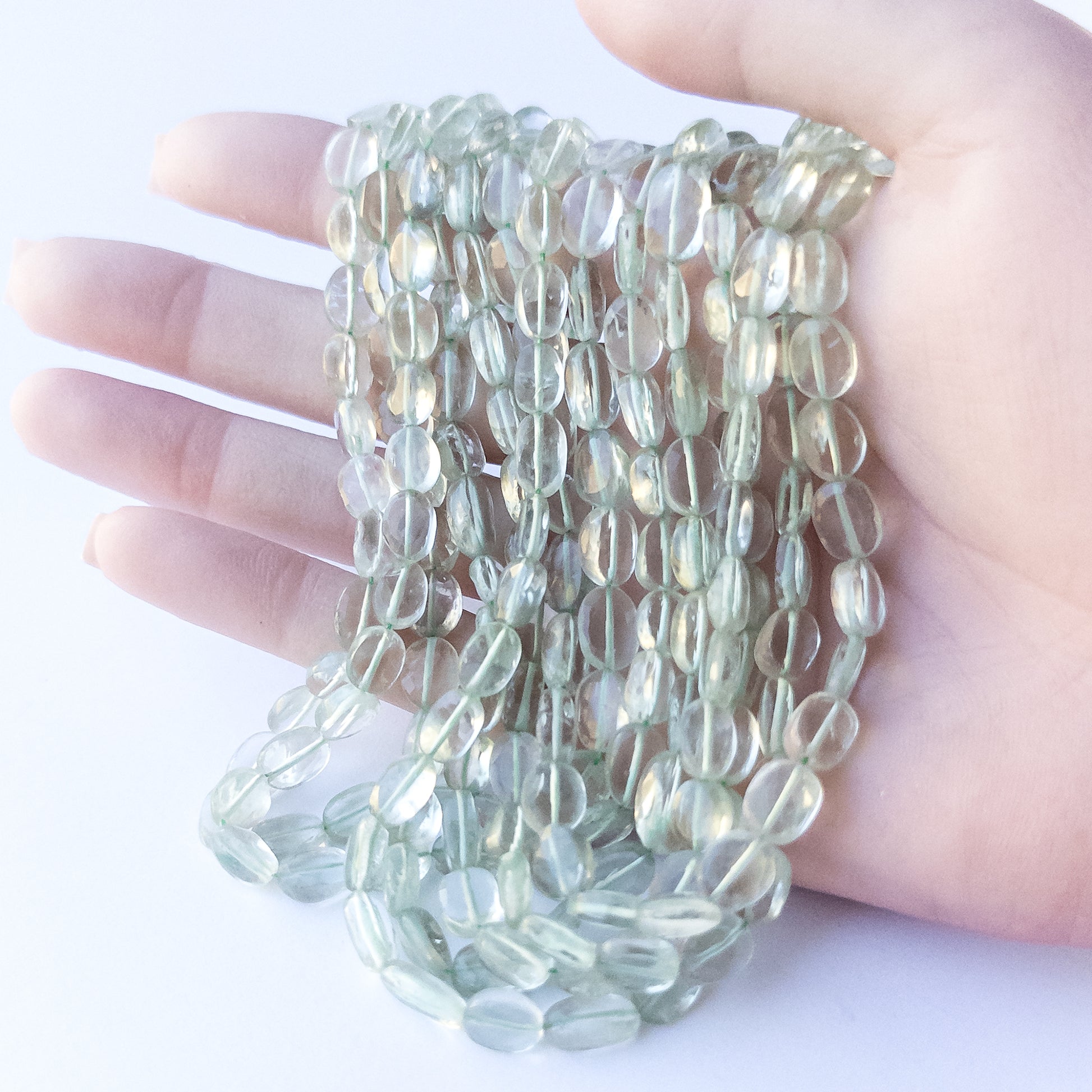A person holds delicate strands of Green Amethyst beads, showcasing their faceted oval design.