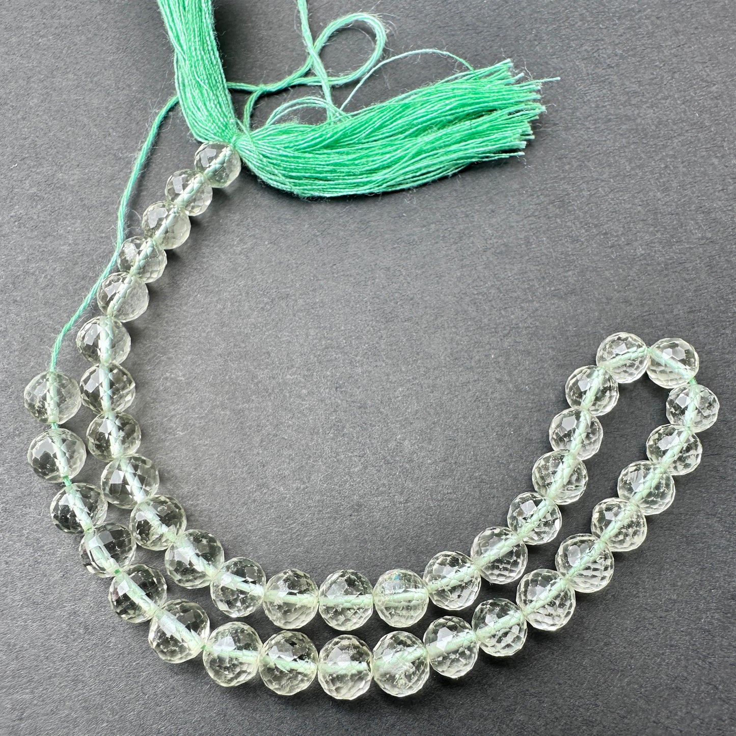 Green Amethyst faceted round beads with soft green tones arranged on a 23cm strand for jewellery making.