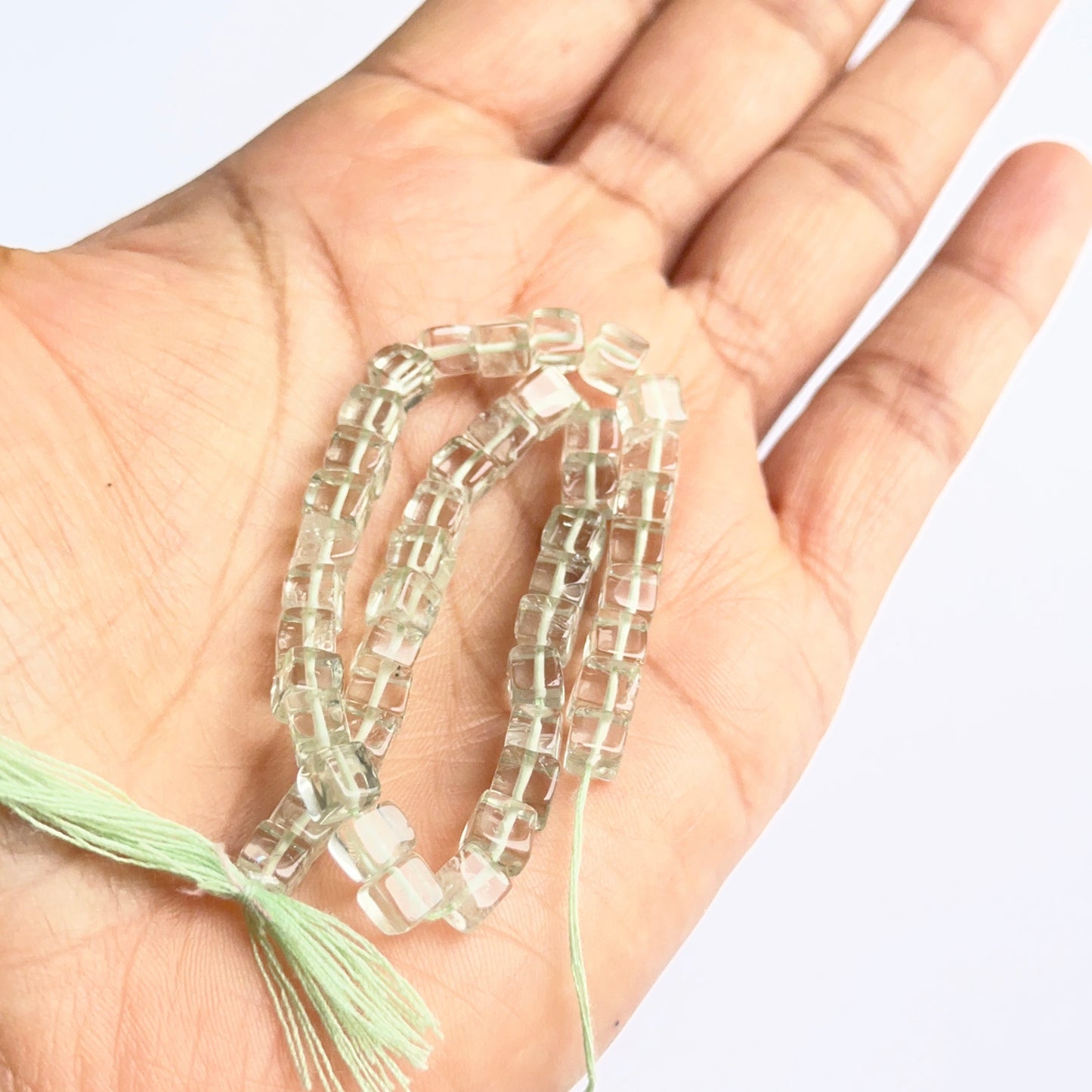 A person holds delicate strands of green amethyst smooth cube beads, showcasing their smooth design.