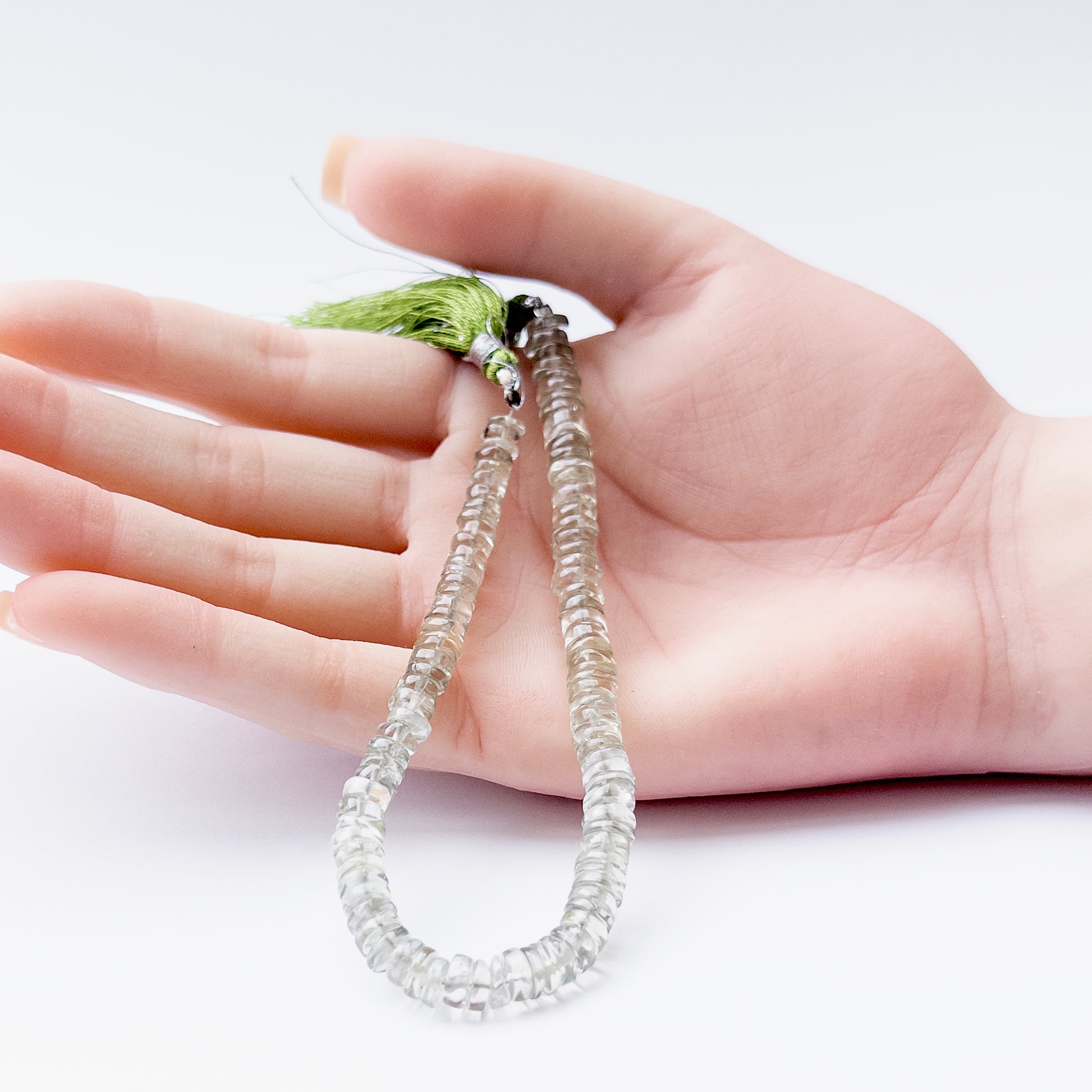 A person holds delicate pieces of Green Amethyst smooth wheel beads, showcasing their shine.