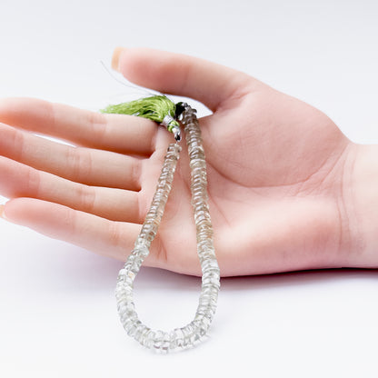 A person holds delicate pieces of Green Amethyst smooth wheel beads, showcasing their shine.