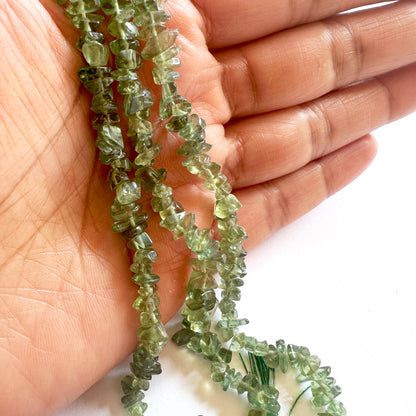 Green apatite gemstone beads held in a hand against a white background
