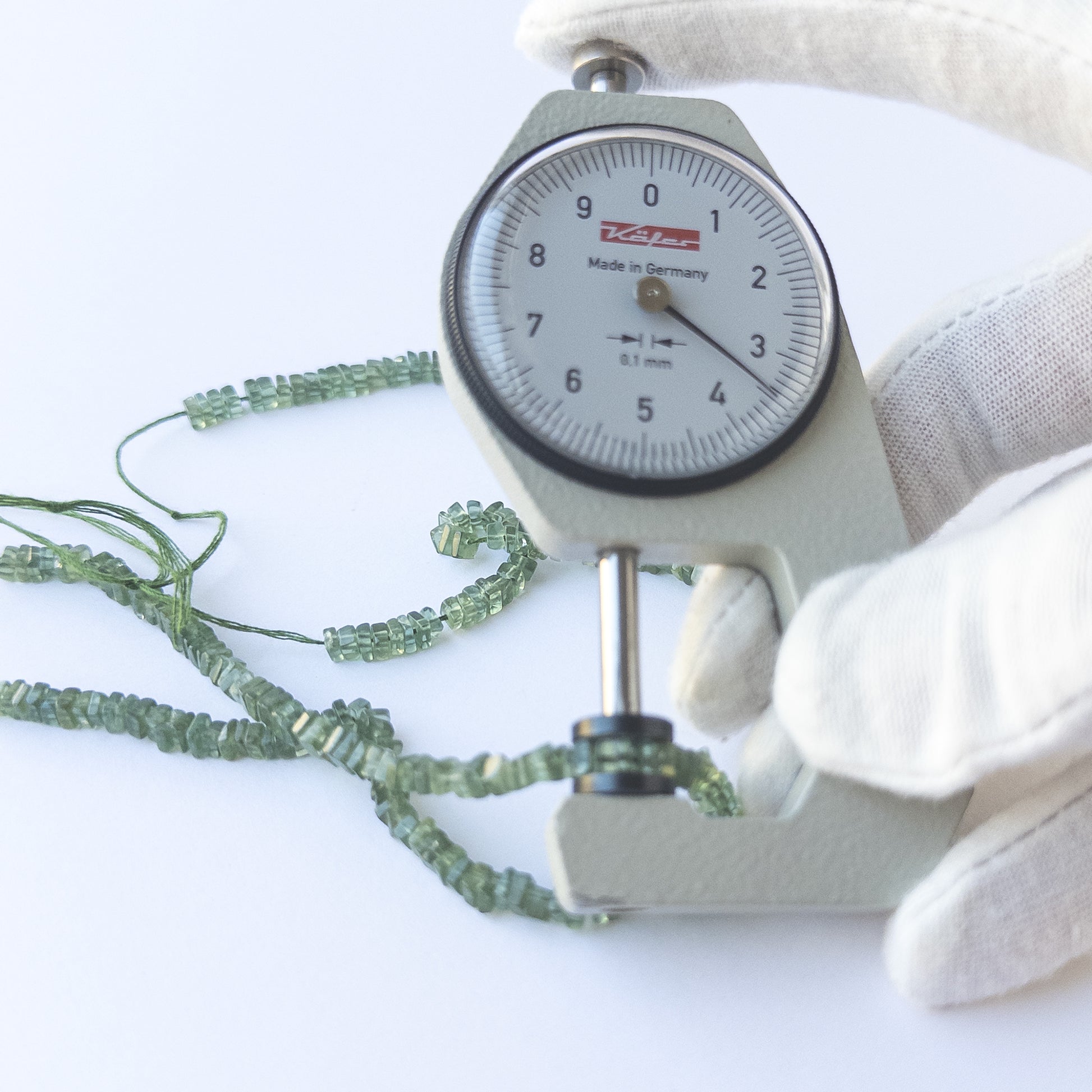 A dial gauge measures the Green Apatite smooth heishi 3.4–3.6mm gemstone.