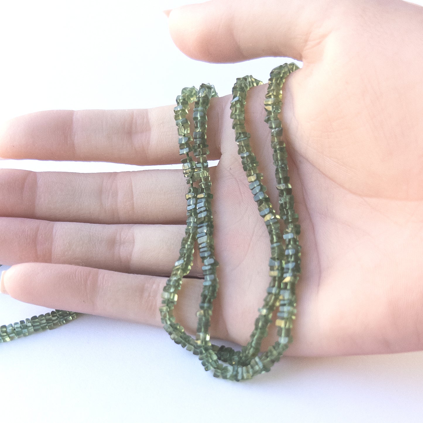 A person holds delicate strands of Green Apatite beads, showcasing their smooth heishi design.