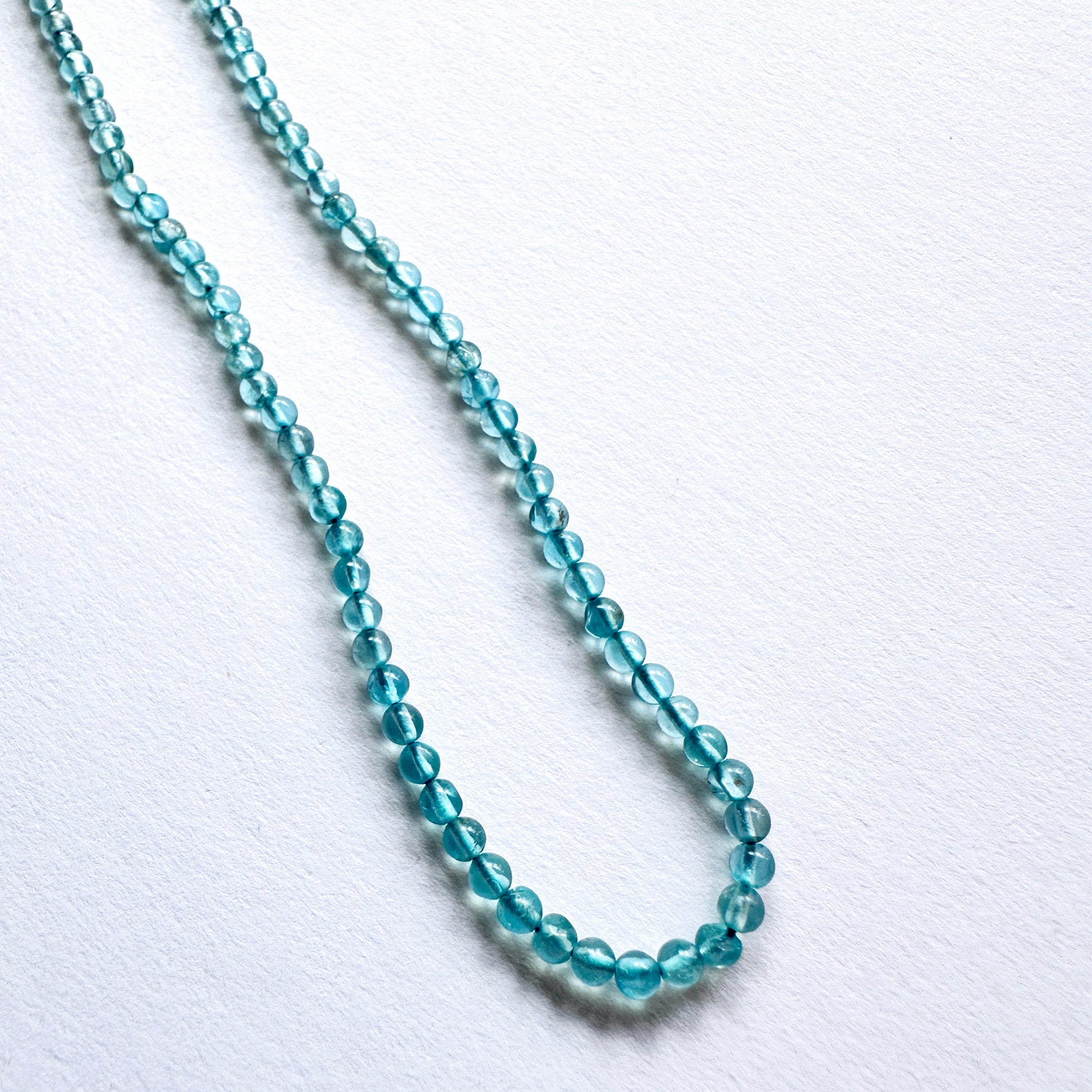 Close-up of 3mm Green Apatite beads arranged on a strand, showcasing clarity and colour.