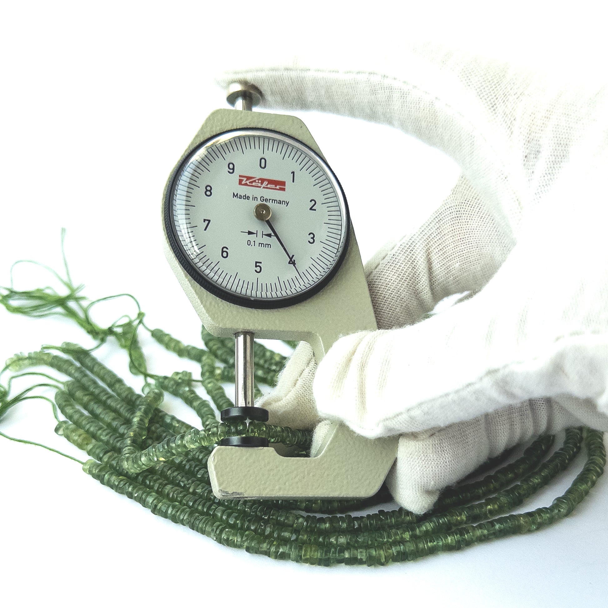 A dial gauge measures the Green Apatite smooth wheel 4mm gemstone.