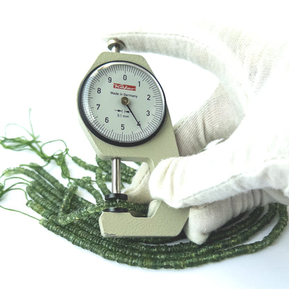 A dial gauge measures the Green Apatite smooth wheel 4mm gemstone.
