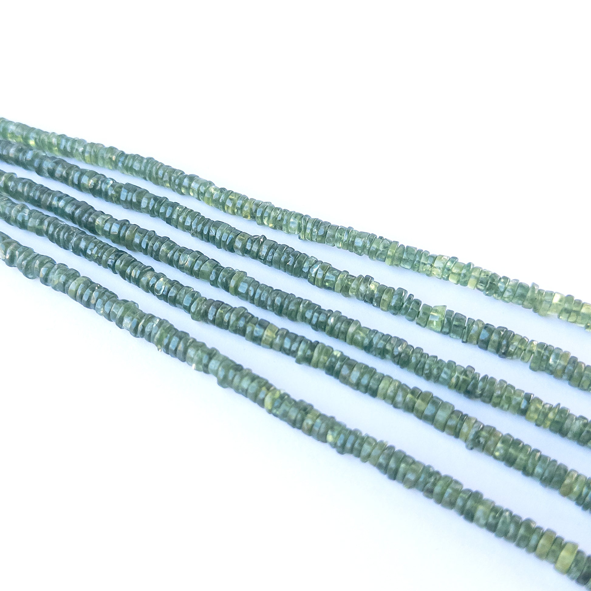 Close‑up of Green Apatite smooth wheel beads showing their glow, cut precision and bright green translucency.
