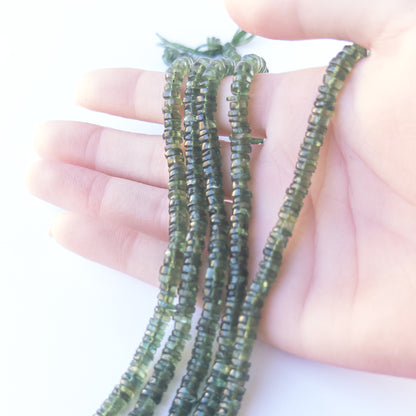 A person holds delicate strands of Green Apatite beads, showcasing their smooth wheel design.