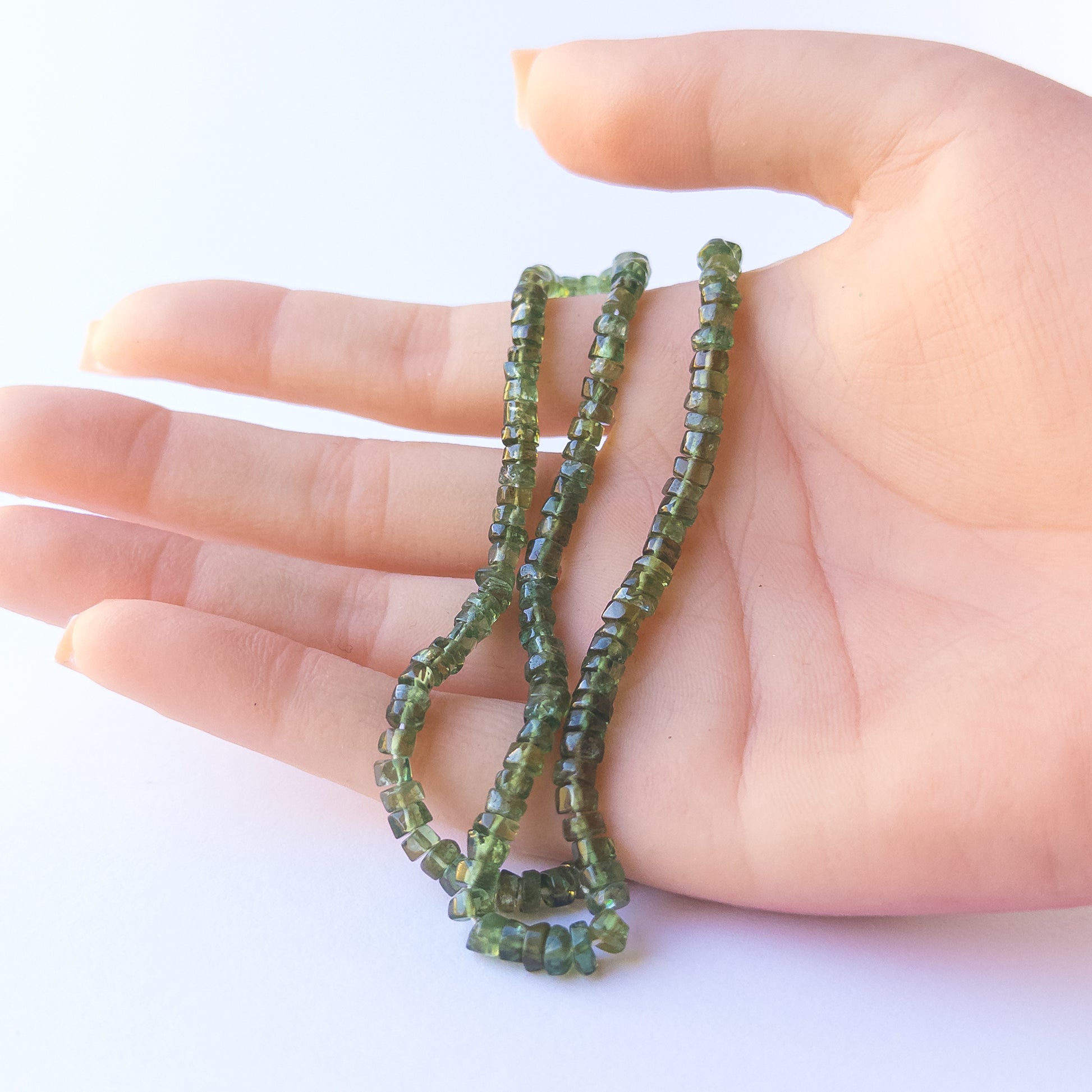 A person holds delicate strands of Green Apatite beads, showcasing their smooth wheel design.
