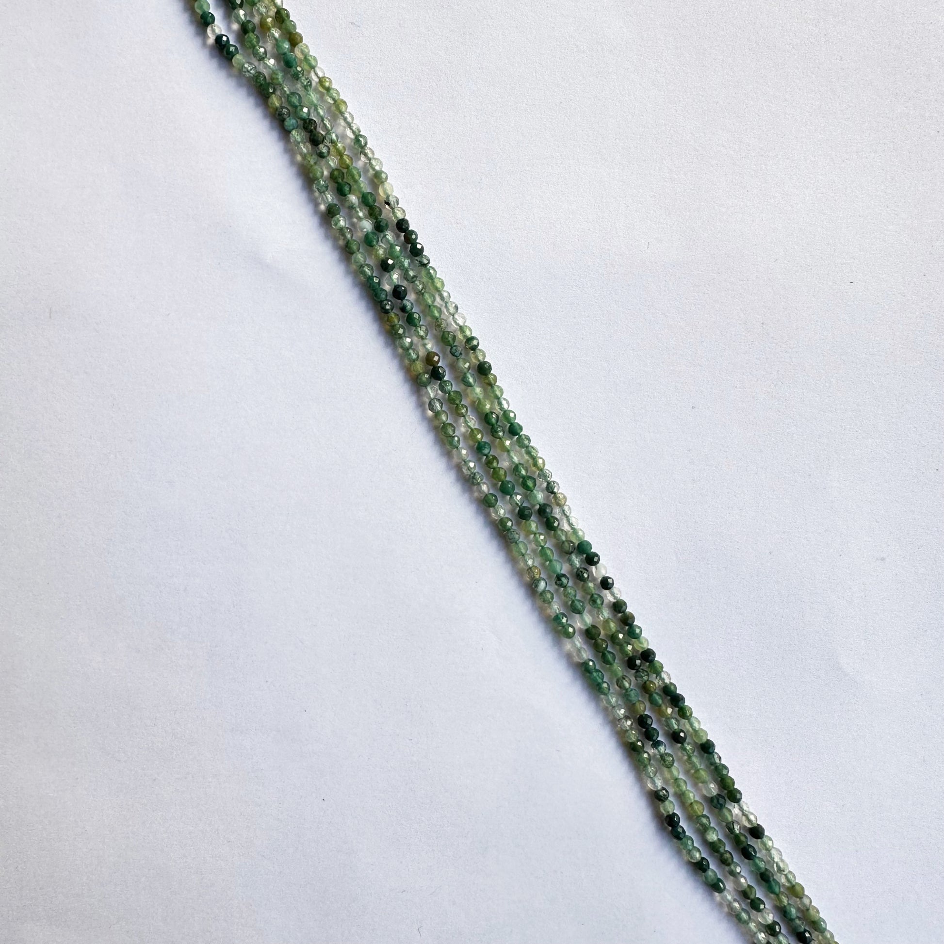 Strands of green aventurine beads coiled together, showing their soft green colour and faceted shine.