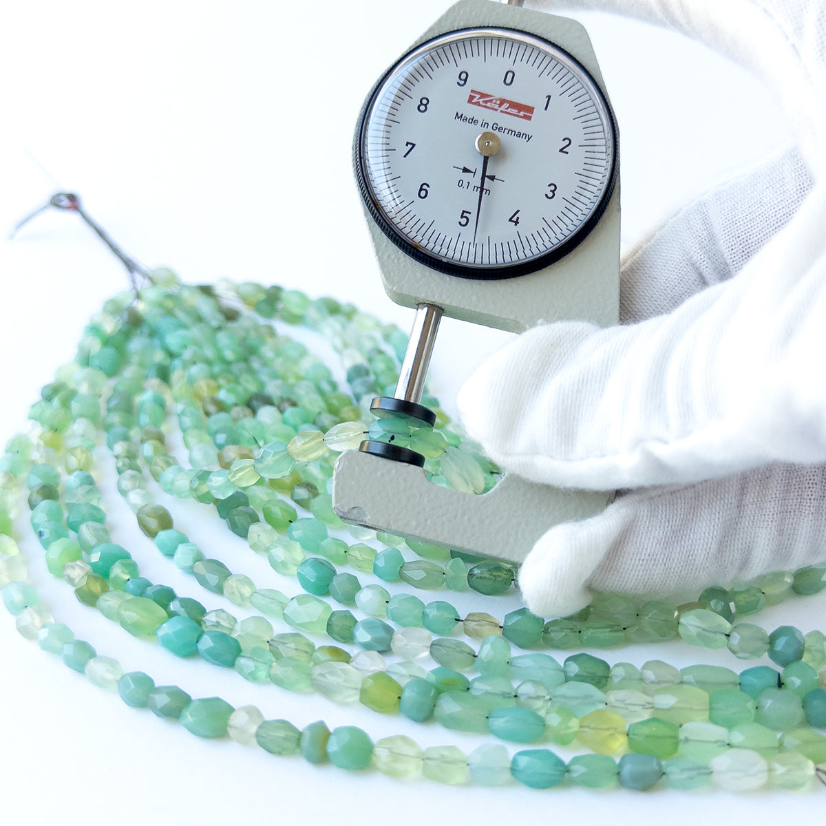 A dial gauge measures the Green Chalcedony faceted oval 4.2–5mm gemstone.
