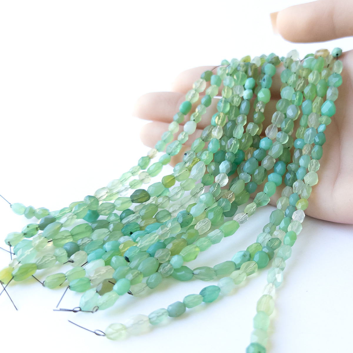 A person holds delicate strands of Green Chalcedony beads, showcasing their faceted oval design.