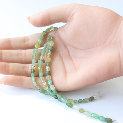 A person holds delicate strands of Green Chalcedony beads, showcasing their faceted oval design.
