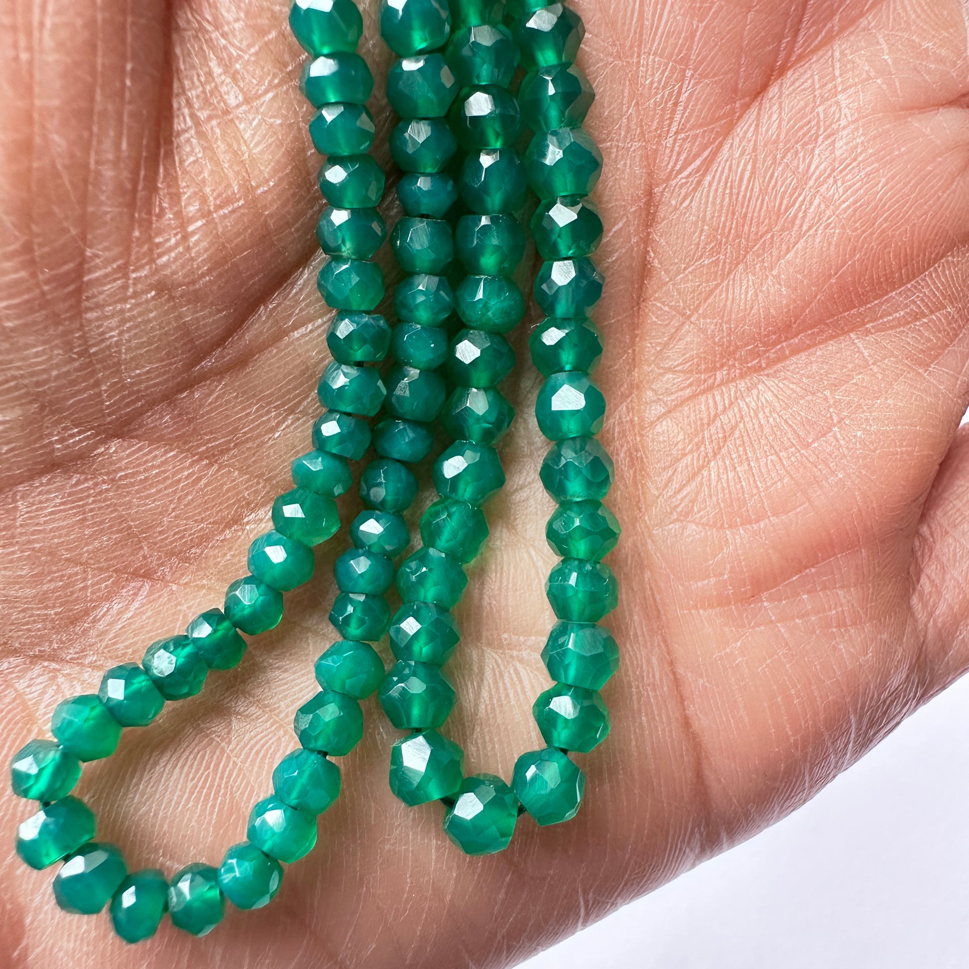 A person holds delicate strands of green onyx beads, showcasing their smooth design.