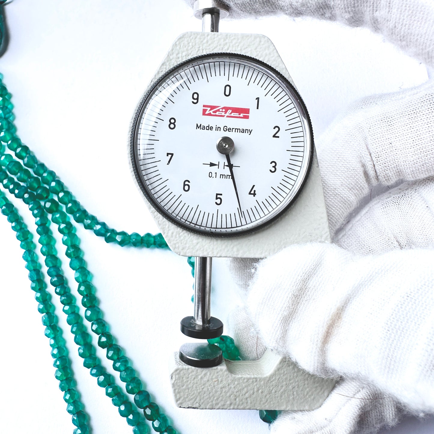 A dial gauge measures the green onyx faceted rondelle gemstone.